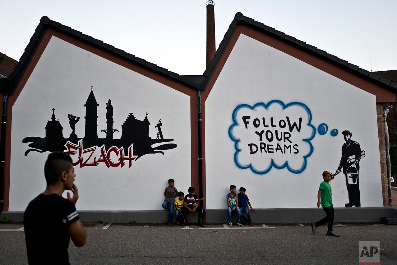  In this Tuesday, Sept. 13, 2016 photo, Dilshad Qasu, 18, left, a Yazidi migrant from Sinjar, Iraq, calls his younger brother Dildar, 11, center, as he sits with other children in a street near their apartment in Elzach, Germany. (AP Photo/Muhammed M