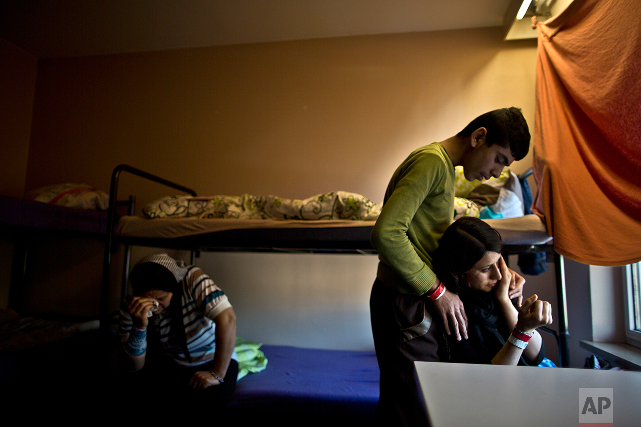  In this Thursday, Dec. 10, 2015 photo, Delphine Qasu, 18, right, a Yazidi refugee from Sinjar, Iraq, is comforted by her brother Dilshad, 17, while crying after talking about their journey to reach Germany, at their new temporary home at Patrick Hen