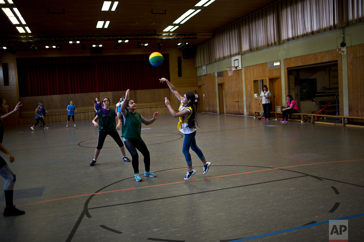  In this Thursday, Sept. 15, 2016 photo, Dunia  Qasu, 14, center, a Yazidi migrant from Sinjar, Iraq, throws the ball while she and her classmates practice basketball during a sport class at her school, Schulzentrum Oberes Elztal, in Oberwinden, Germ