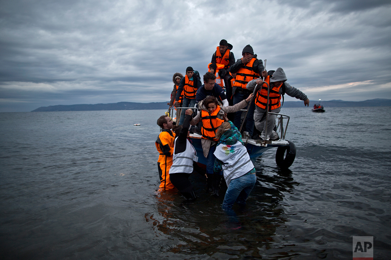 In this Thursday, Dec. 3, 2015 photo, volunteers help refugees disembark from a vessel carrying Yazidi refugee Samir Qasu, 45, from Sinjar, Iraq, and his wife Bessi, 42, their two daughters Delphine, 18, seen center left, Dunia 13, and their two sons Dilshad, 17, seen center left, and Dildar, 10, as it arrives to the northeastern Greek island of Lesbos from the Turkish coast. (AP Photo/ Muhammed Muheisen)