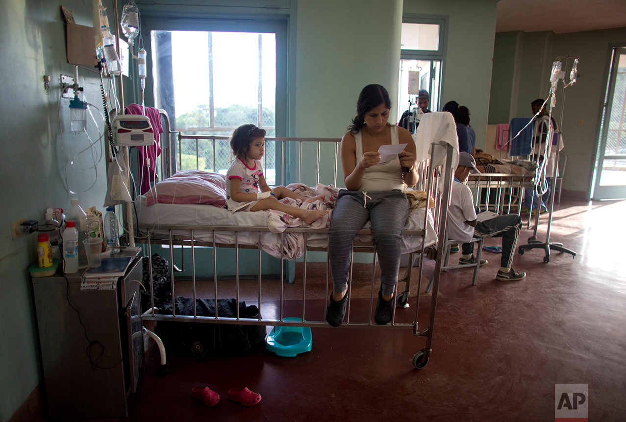 In this Aug. 16, 2016 photo, 3-year-old Ashley sits on her hospital bed as her mother Oriana Pacheco reads a prescription, at University Hospital in Caracas, Venezuela. Ashley’s parents not only maxed out their credit cards and borrowed as much money as they could from family to pay for scarce antibiotics, but they were eating just one meal a day, sold their fridge, television, Oriana’s cellphone and their children’s Play Station. (AP Photo/Ariana Cubillos)