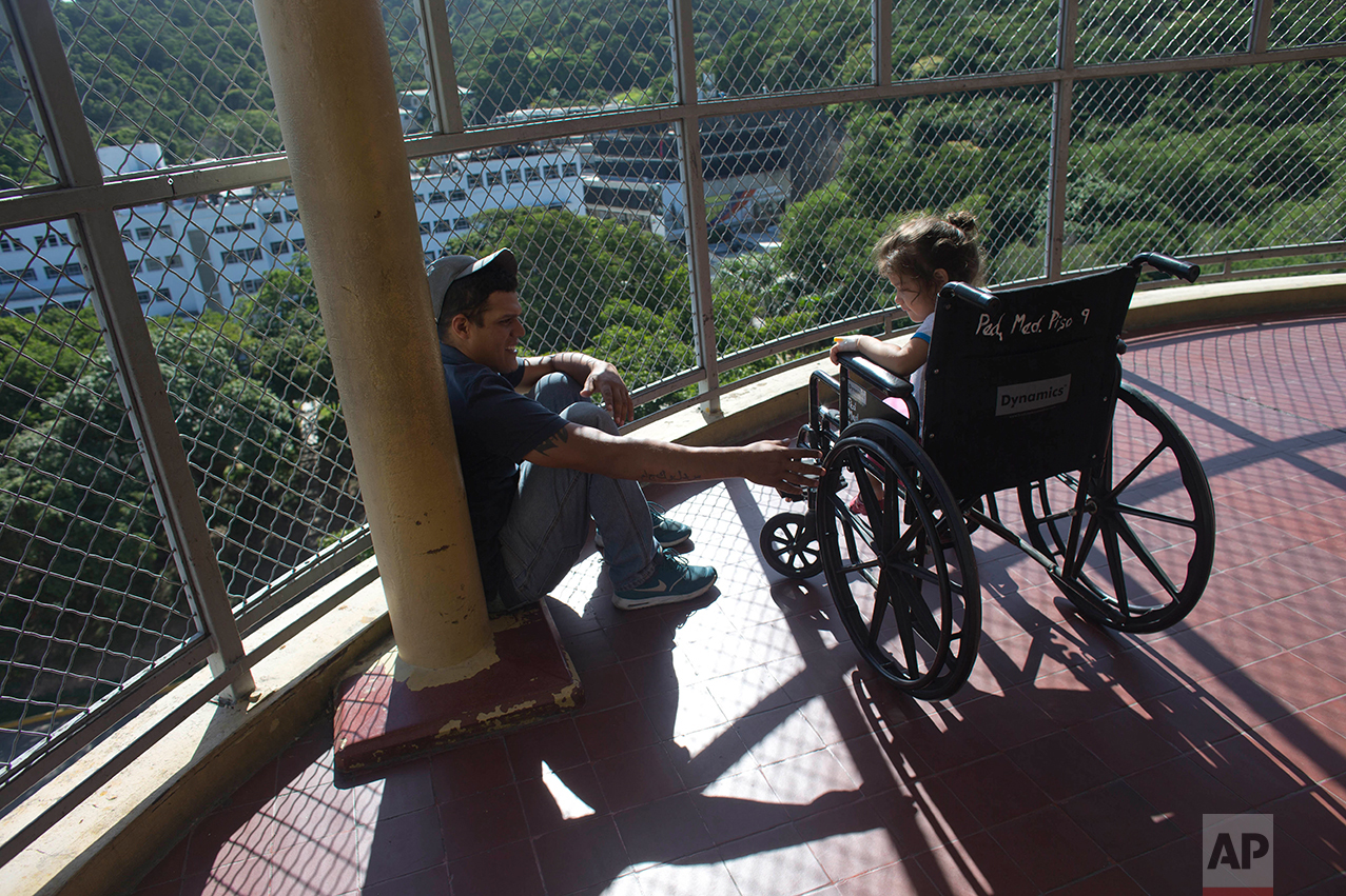 In this Aug. 17, 2016 photo, Maykol Pacheco sits with his 3-year-old daughter Ashley, who is recovering from a staph infection, on a balcony at University Hospital in Caracas, Venezuela. Out of options, Pacheco brought his daughter to University Hospital, once one of the best hospitals in South America but lately better known for gang shootings in the operating rooms and stickups in the stairways. (AP Photo/Ariana Cubillos)