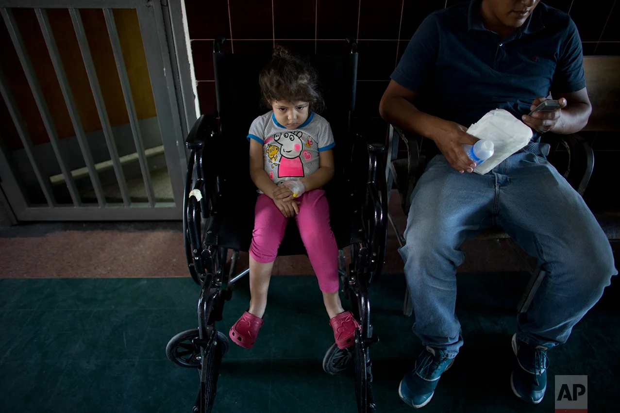 In this Aug. 17, 2016 photo, 3-year old Ashley Pacheco waits with her father Maykol to have her stitches removed from her left leg, at University Hospital in Caracas, Venezuela. Two weeks after Ashley scraped her knee, she was screaming in a hospital, fighting for her life as her family scoured Caracas for scarce antibiotics. When she arrived at the hospital Ashley's left leg had swollen from the tip of her toe to the top of her thigh. (AP Photo/Ariana Cubillos)