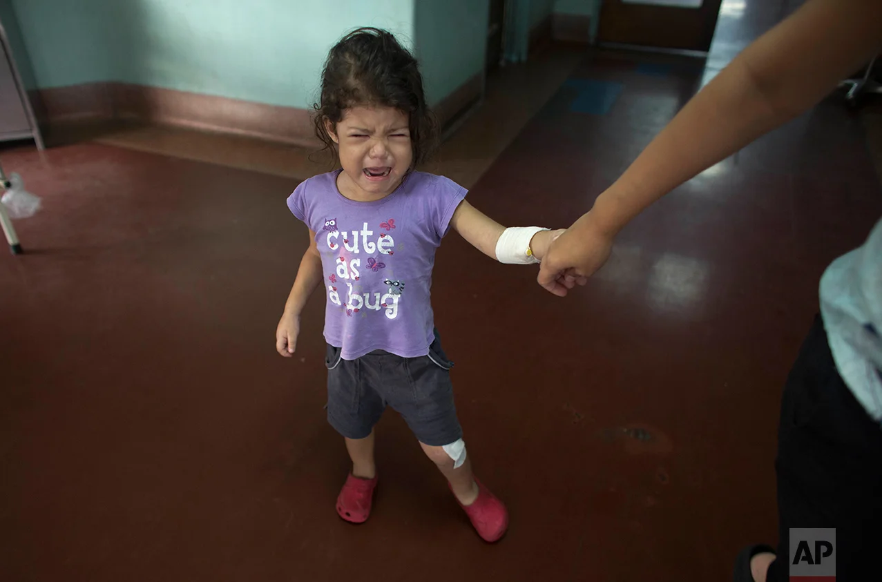 In this Aug. 23, 2016 photo, 3-year-old Ashley Pacheco cries from the pain walking causes in her left leg, as she holds on to her mother’s hand, at University Hospital in Caracas, Venezuela. Ashley's parents had been determined to shield her from the chaos engulfing their country. As the public school system collapsed , they sent her to a private Catholic preschool. As food grew harder to find, they made sure she had protein at every meal. When water began coming out of the taps with a foul smell, they boiled it before her daily bath. But their real troubles began when Ashley’s scraped knee led to a staph infection. (AP Photo/Ariana Cubillos)