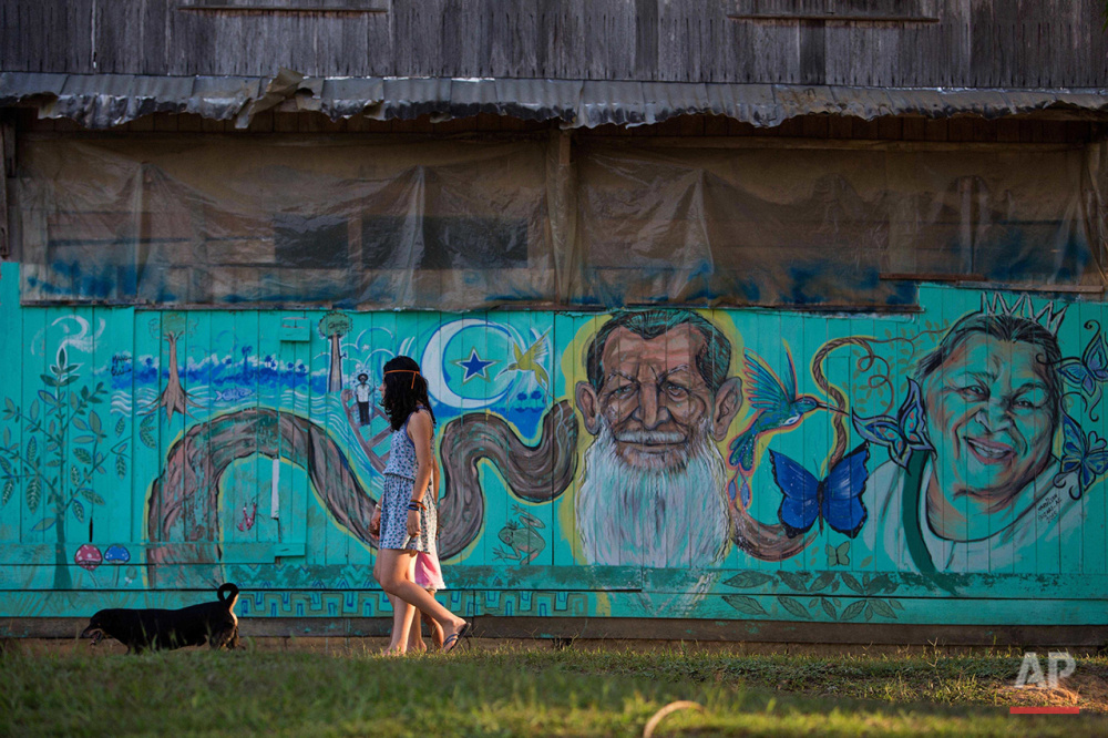  In this June 23, 2016 photo, girls walk in front of a mural with images of the founder of the Ceu do Mapia community, Godfather Sebastiao, and his wife Godmother Rita, at Ceu do Mapia, Amazonas state, Brazil. In the early 1980s rubber tapper Sebasti