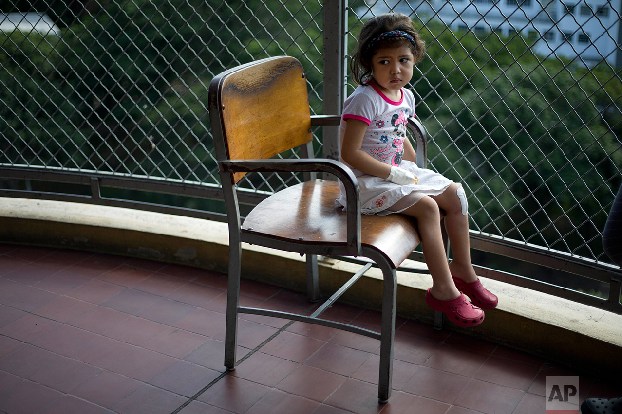 In this Aug. 16, 2016 photo, Ashley Pacheco sits in a chair on a balcony at University Hospital in Caracas, Venezuela. Two weeks after the 3-year-old scraped her knee, she was screaming in a hospital, fighting for her life as her family scoured Caracas for scarce antibiotics. (AP Photo/Ariana Cubillos)