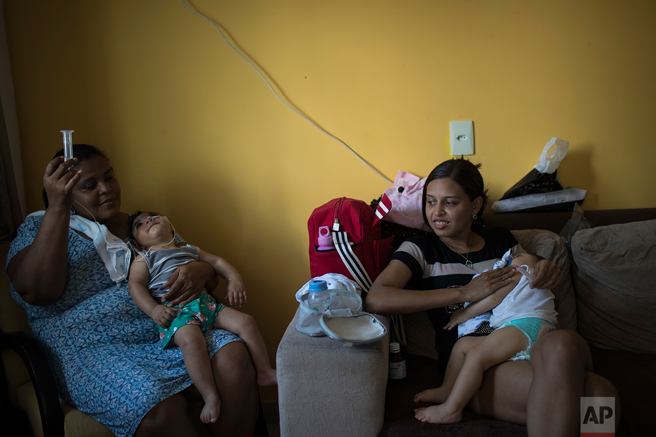 In this Oct. 1, 2016 photo, Daniele Ferreira dos Santos and her son Juan Pedro, right, sit next to Heloisa Dias who feeds her grandson Arthur Conceicao during his one-year birthday party in Recife, Pernambuco state, Brazil. Arthur, who was born with microcephaly, has started taking high-calorie formula through a tube after he appeared to choke during meals. (AP Photo/Felipe Dana)