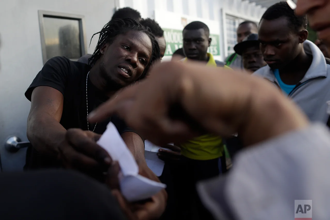 In this Sept. 27, 2016 photo, Haitian migrants speak with Mexican officials as they hope to gain a spot on the daily list to pass to the U.S. side of the border crossing, in Tijuana, Mexico. Once inside the United States, the Haitians cannot be returned back to Mexico. They are held in U.S. detention centers pending repatriation. (AP Photo/Gregory Bull)