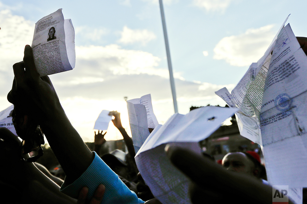In this Sept. 27, 2016 photo, Haitian migrants hold up their Mexican migration documents as they hope to gain a spot on the daily list to cross to the U.S. side of the border, in Tijuana, Mexico. With hundreds, perhaps thousands, of Haitian men, women and young children regularly spending the night just outside the busiest United States border crossing, Mexican officials have moved to bring some order to the unruly scene by granting 20-day permits to stay in Mexico while also helping schedule their slots with the Americans on the other side. (AP Photo/Gregory Bull)
