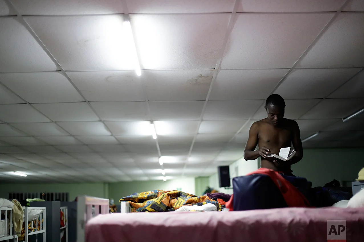 In this Sept. 26, 2016 photo, a Haitian migrant reads a Bible at the Padre Chava migrant shelter, in Tijuana, Mexico. Padre Chava, one of 10 Tijuana shelters that house Haitians, turned away hundreds over the weekend, leading many to sleep outside on cardboard sheets. (AP Photo/Gregory Bull)