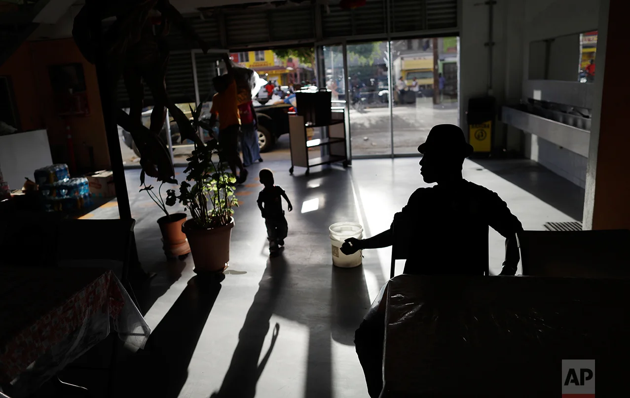 In this Sept. 26, 2016 photo, a Haitian man returns a ball to a boy at the Padre Chava migrant shelter, in Tijuana, Mexico. Padre Chava, one of 10 Tijuana shelters that house Haitians, turned away hundreds over the weekend, leading many to sleep outside on cardboard sheets. (AP Photo/Gregory Bull)