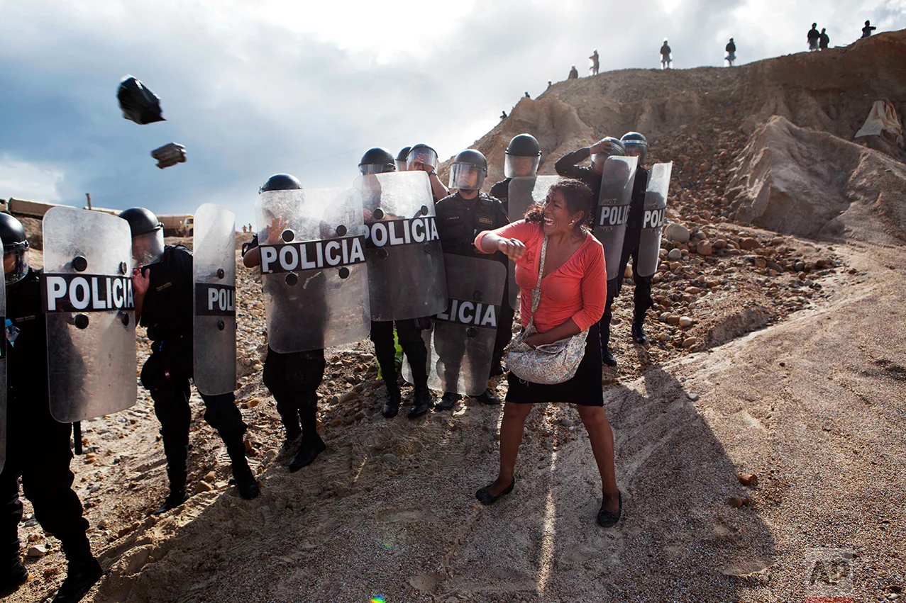  In this April 28, 2014 photo, a woman throws a rock and a bag at riot policemen who block her way home in Huepetuhe district in Peru's Madre de Dios region in Peru. Authorities began enforcing a ban on illegal mining in the Huepetuhe district, and before the deadline, miners clashed with police while intermittently blocking traffic on the Interoceanic Highway that links the Pacific with Brazil. (AP Photo/Rodrigo Abd)