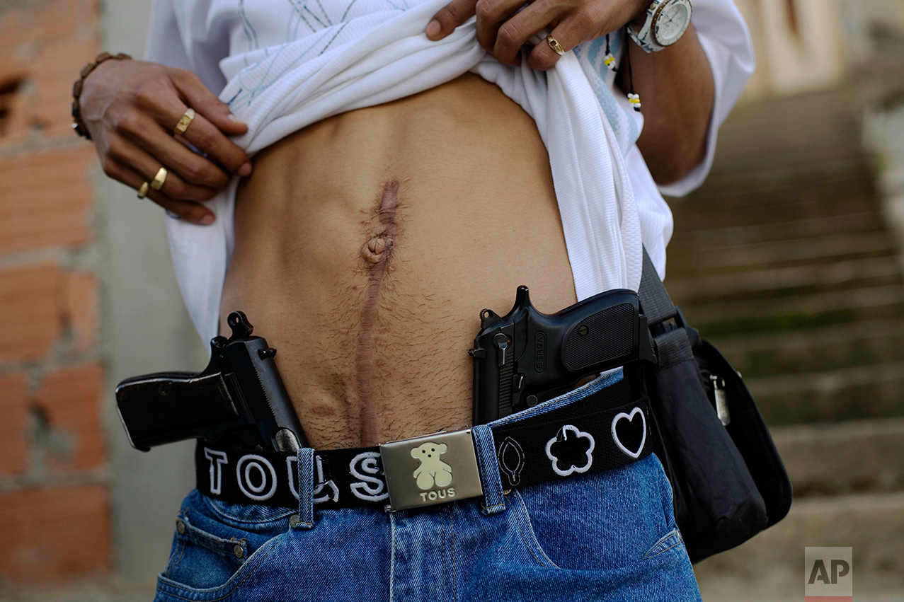 In this Nov. 25, 2007 photo, drug dealer Joan, who identifies himself as "El Patan," shows his guns and a scar on his stomach from an injury suffered during clashes with rival gangs in Las Mayas neighborhood in Caracas, Venezuela. (AP Photo/Rodrigo Abd)