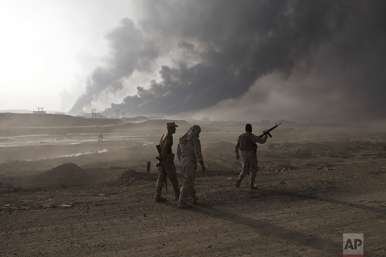 Iraqi army soldiers man a checkpoint as oil wells burn on the outskirts of Qayyarah, Iraq, Wednesday, Oct. 19, 2016. A senior Iraqi general on Wednesday called on Iraqis fighting for the Islamic State group in Mosul to surrender as a wide-scale operation to retake the militant-held city entered its third day. (AP Photo/Marko Drobnjakovic)