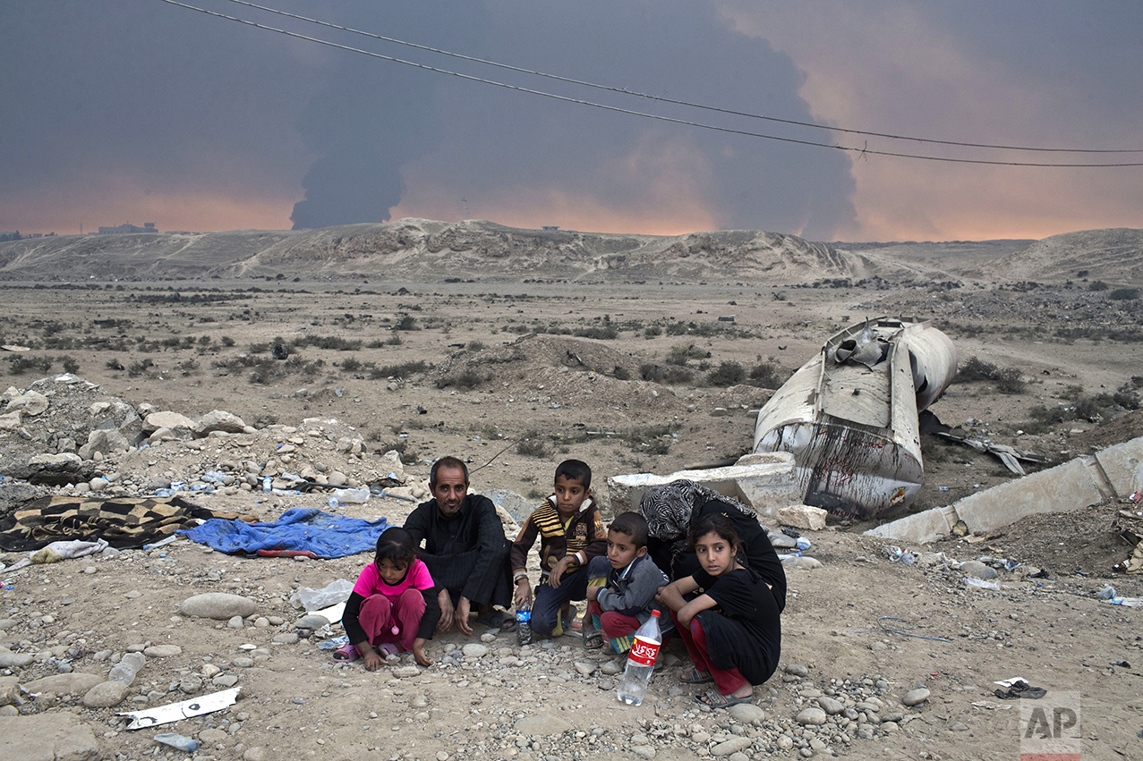 Internally displaced persons sit at a checkpoint as smoke rises from the burning oil wells in Qayyarah, about 31 miles (50 km) south of Mosul, Iraq, Sunday, Oct. 23, 2016. Islamic State fighters torched a sulfur plant south of Mosul, sending a cloud of toxic fumes into the air that mingled with oil wells the militants had lit on fire to create a smoke screen. (AP Photo/Marko Drobnjakovic)