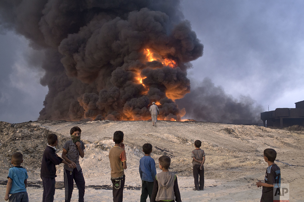 In this Sunday, Oct. 23, 2016 photo, people watch a burning oil well in Qayyarah, about 31 miles (50 km) south of Mosul, Iraq. In the week since Iraq launched an operation to retake Mosul from the Islamic State group, its forces have pushed toward the city from the north, east and south, battling the militants in a belt of mostly uninhabited towns and villages. In the heavily mined approaches to the city they met with fierce resistance, as IS unleashed suicide truck bombs, rockets and mortars. (AP Photo/Marko Drobnjakovic)