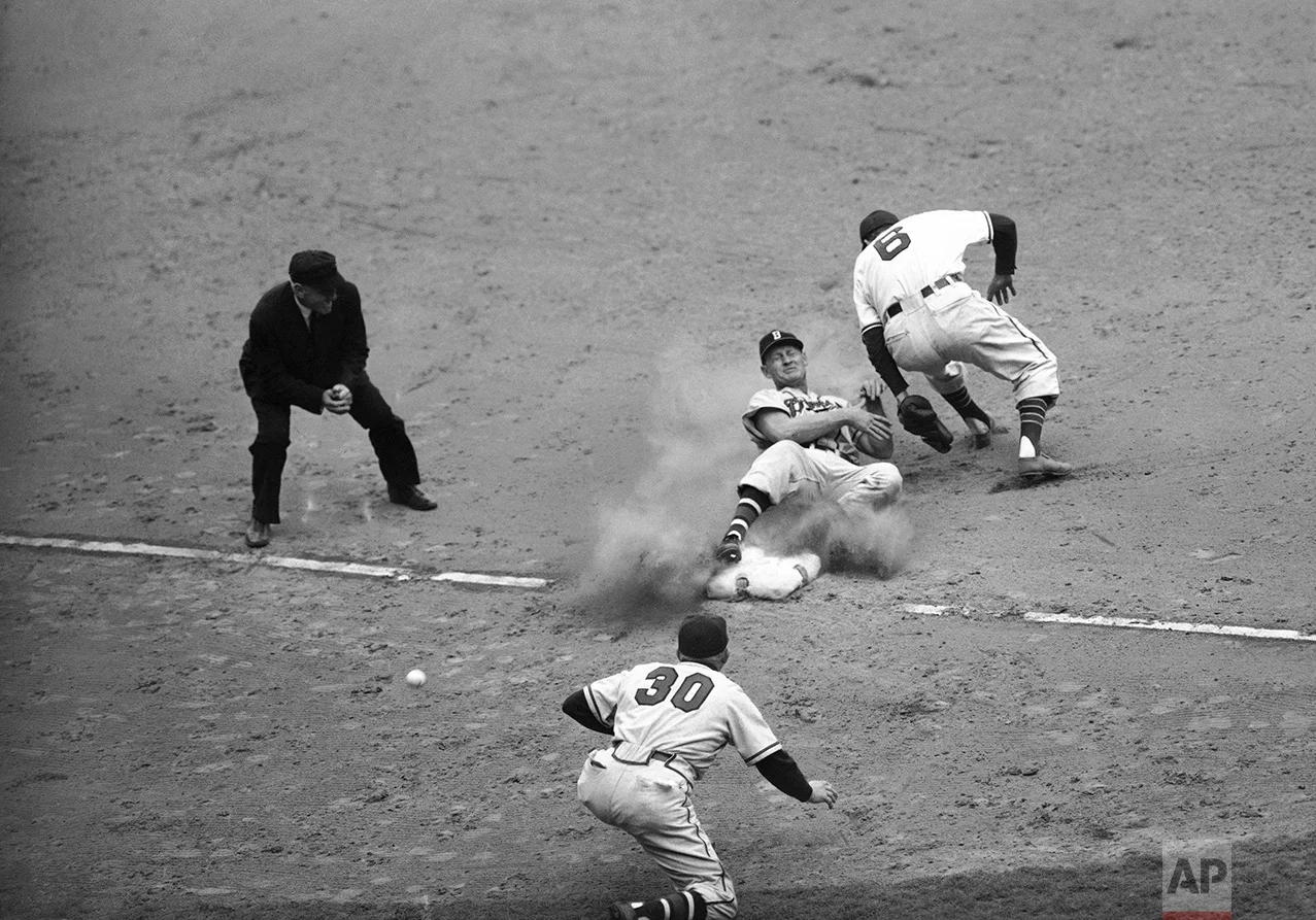 Bob Elliott, Boston third baseman, comes into third base on his back as the ball (lower left) skips past Ken Keltner, Cleveland third baseman, in the seventh inning of the fifth World Series game in Cleveland, Ohio on Oct. 10, 1948. Elliott got up and scored. Manager Billy Southworth (30) is third base coach. (AP Photo)