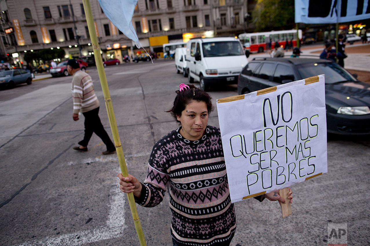 In this Oct. 5, 2016 photo, Ana Paz holds a sign that reads in Spanish "We don't want to be poorer" as she protests outside Congress, near a soup kitchen in Buenos Aires, Argentina. President Mauricio Macri's market-friendly reforms have been praised by international investors, who say they lay the groundwork for growth. But so far, they've brought only pain to the country's poor. (AP Photo/Natacha Pisarenko)