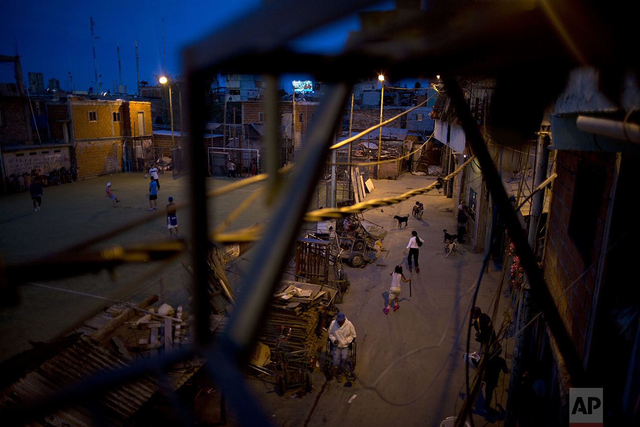 In this Oct. 13, 2016 photo, girls rollerblade past what's left of cars parked in the Villa 31 neighborhood as boys play soccer in Buenos Aires, Argentina. The government says more than 32 percent of Argentines live in poverty. That's up from 29 percent in the 10 months since President Mauricio Macri took office, according to a study by the Catholic University of Argentina. (AP Photo/Natacha Pisarenko)