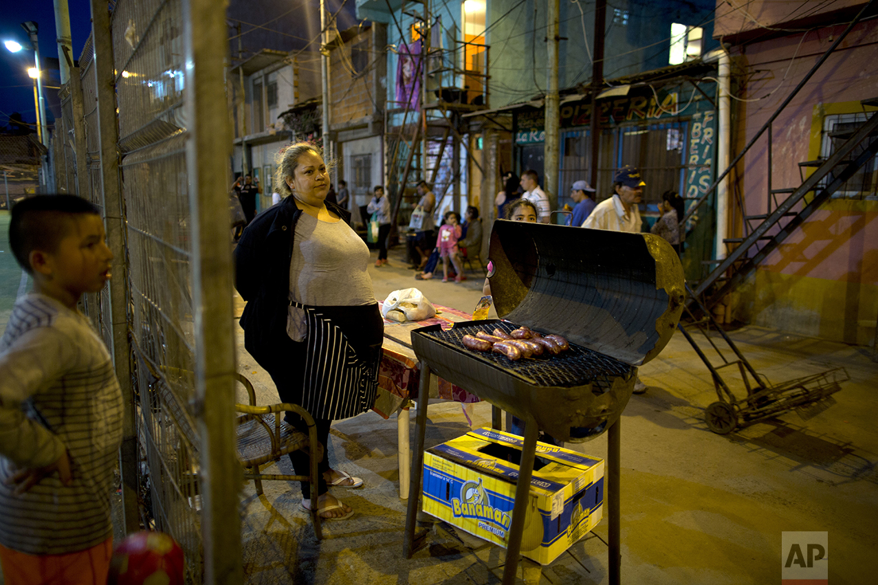 In this Oct. 13, 2016 photo, Miriam Cruz, center, cooks chorizos for meat sandwiches called "choripanes" in the Villa 3 neighborhood of Buenos Aires, Argentina. Since her husband lost his job four months ago, Cruz has been the only breadwinner in her family of four, and her two daughters line up every night outside the soup kitchen because they can no longer afford dinner. (AP Photo/Natacha Pisarenko)