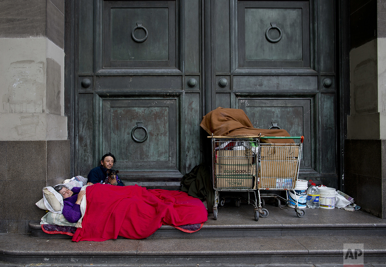 In this Oct. 5, 2016 photo, Maria Susana Silveira, 55, and Jorge Fernandez, 46, who live in the street as a team, rest outside Banco Nacion with their dog Toto, across the street from La Casa Rosada presidential house in Buenos Aires, Argentina. "In the past nine months, about 1.5 million people have joined the ranks of the poor," said Lucila de Ponti, an opposition lawmaker leading the fight for a stimulus bill meant to create 1 million jobs. (AP Photo/Natacha Pisarenko)