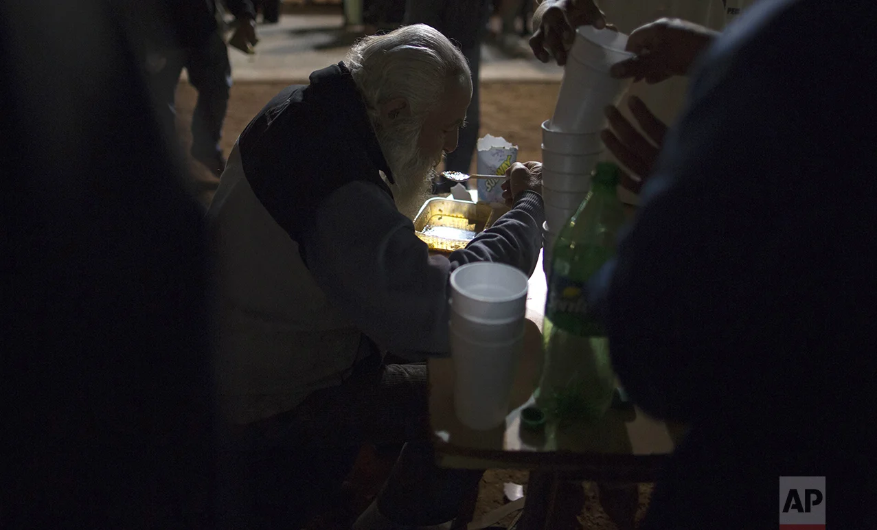 In this Oct. 5, 2016 photo, a homeless man eats free dinner at a soup kitchen set up on the sidewalk outside Congress in Buenos Aires, Argentina. Organizers set up their soup kitchen outside the legislature to make as statement to the government about poverty in the city. (AP Photo/Natacha Pisarenko)