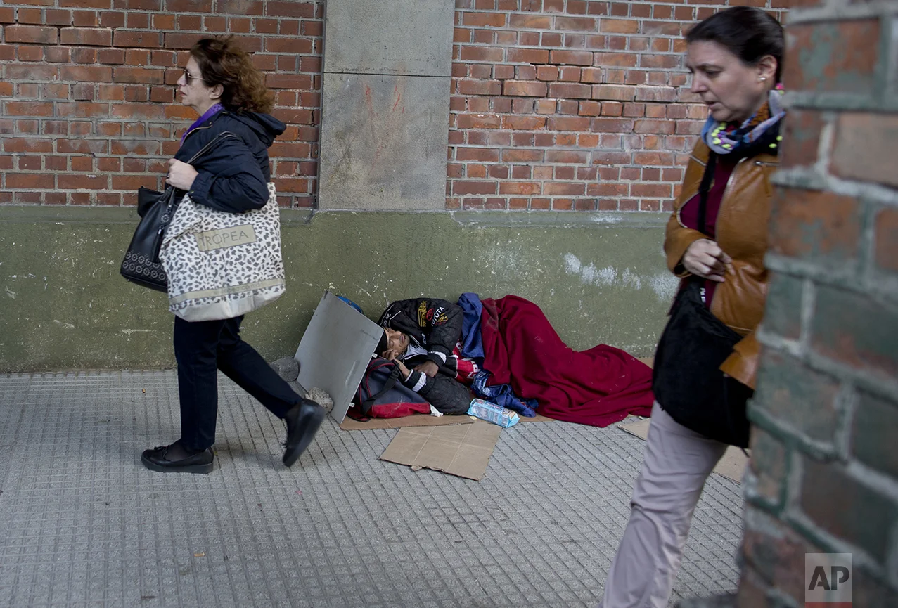 In this Oct. 4, 2016 photo, women walk by a man sleeping on the sidewalk in Buenos Aires, Argentina. As President Mauricio Macri campaigned last year, he often said his goal was to reach "zero poverty" by the end of his term in 2019. But when he released the poverty figures in late September, he said it's obvious it won't be possible. (AP Photo/Natacha Pisarenko)