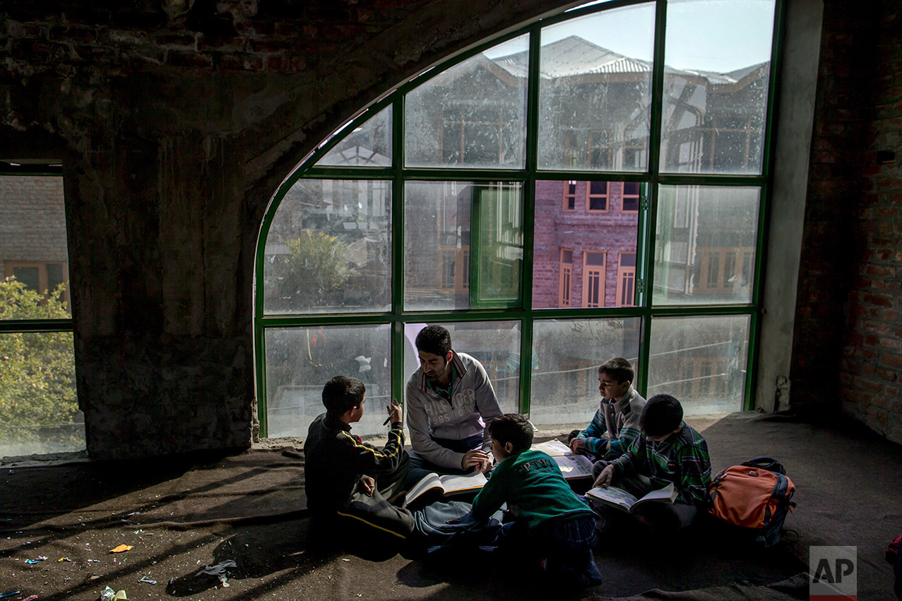 In this Thursday, Oct. 20, 2016 photo, Faheel Abbas teaches Kashmiri children in an ad-hoc learning center at a local mosque in Srinagar, Indian controlled Kashmir. With daily life still paralyzed by strikes and rolling curfews, dozens of learning centers have popped up in people's homes or religious centers like mosques in Kashmir since August. They gather during daylight hours, often sitting on the floor, to hear a teacher read aloud from a text or practice mathematical equations in a shared notebook. (AP Photo/Dar Yasin)