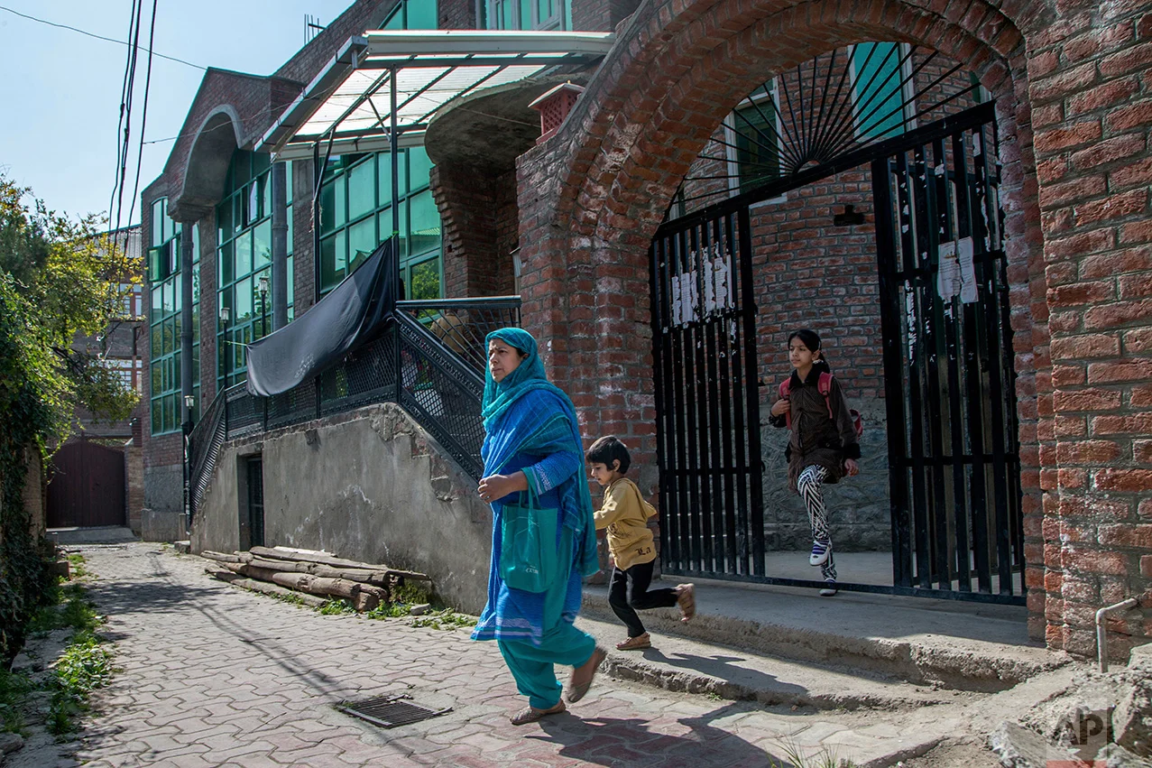 In this Thursday, Oct. 20, 2016 photo, a Kashmiri woman walks home with her children after attending alternate classes set up at a local mosque in Srinagar, Indian controlled Kashmir. With daily life still paralyzed by strikes and rolling curfews, dozens of ad-hoc learning centers have popped up in people's homes or religious centers like mosques in Kashmir since August. The centers are doing more than just helping students prepare for upcoming exams, organizers said. They're keeping kids off the streets and giving them comfort amid a civilian uprising sparked when a popular rebel leader was killed in fighting Indian forces on July 8. (AP Photo/Dar Yasin)