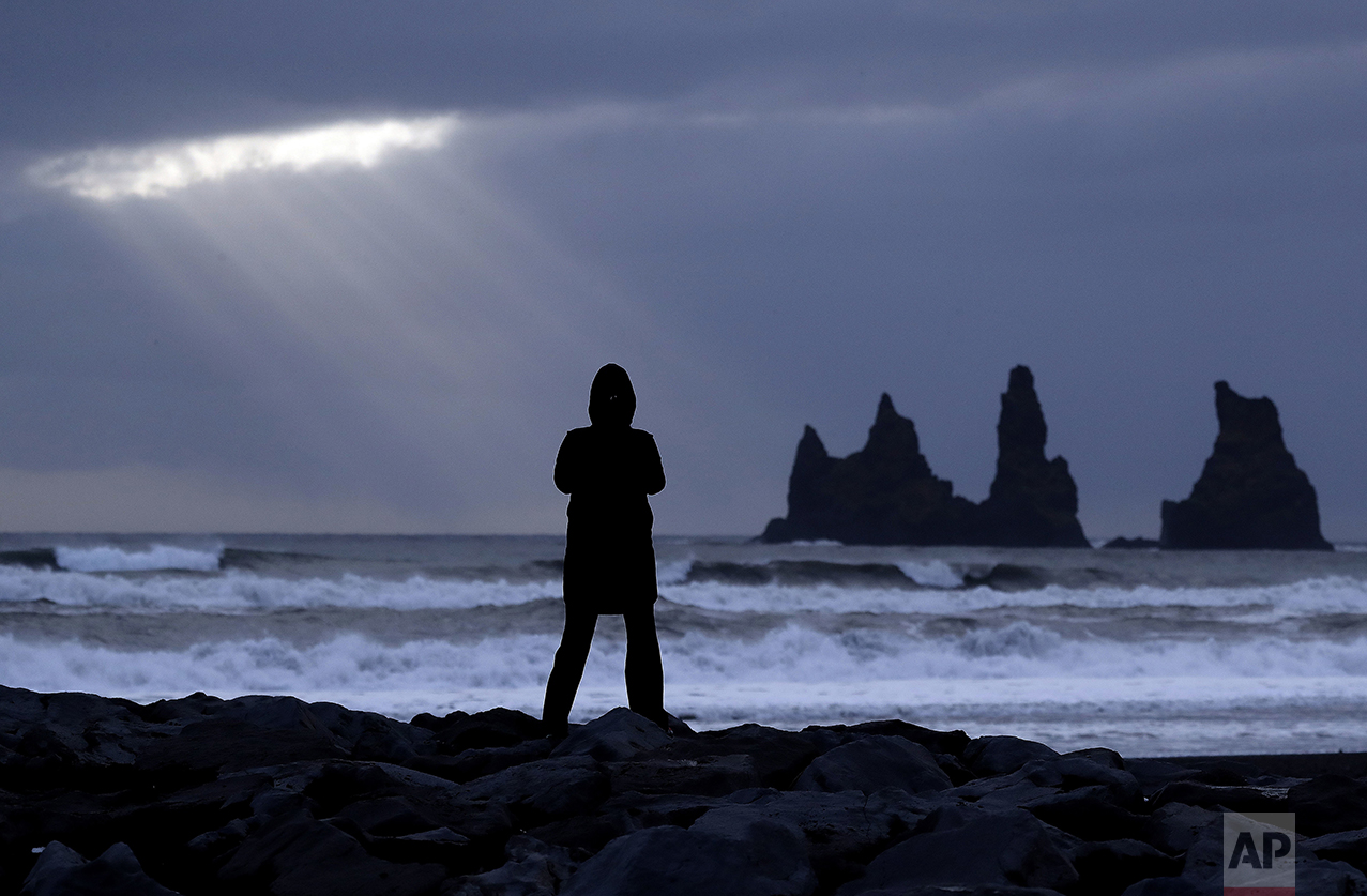  The sun shines through clouds as a woman stands on a black sand beach in Vik, Iceland, near the Volcano Katla, on Friday, Oct. 28, 2016. (AP Photo/Frank Augstein) 
