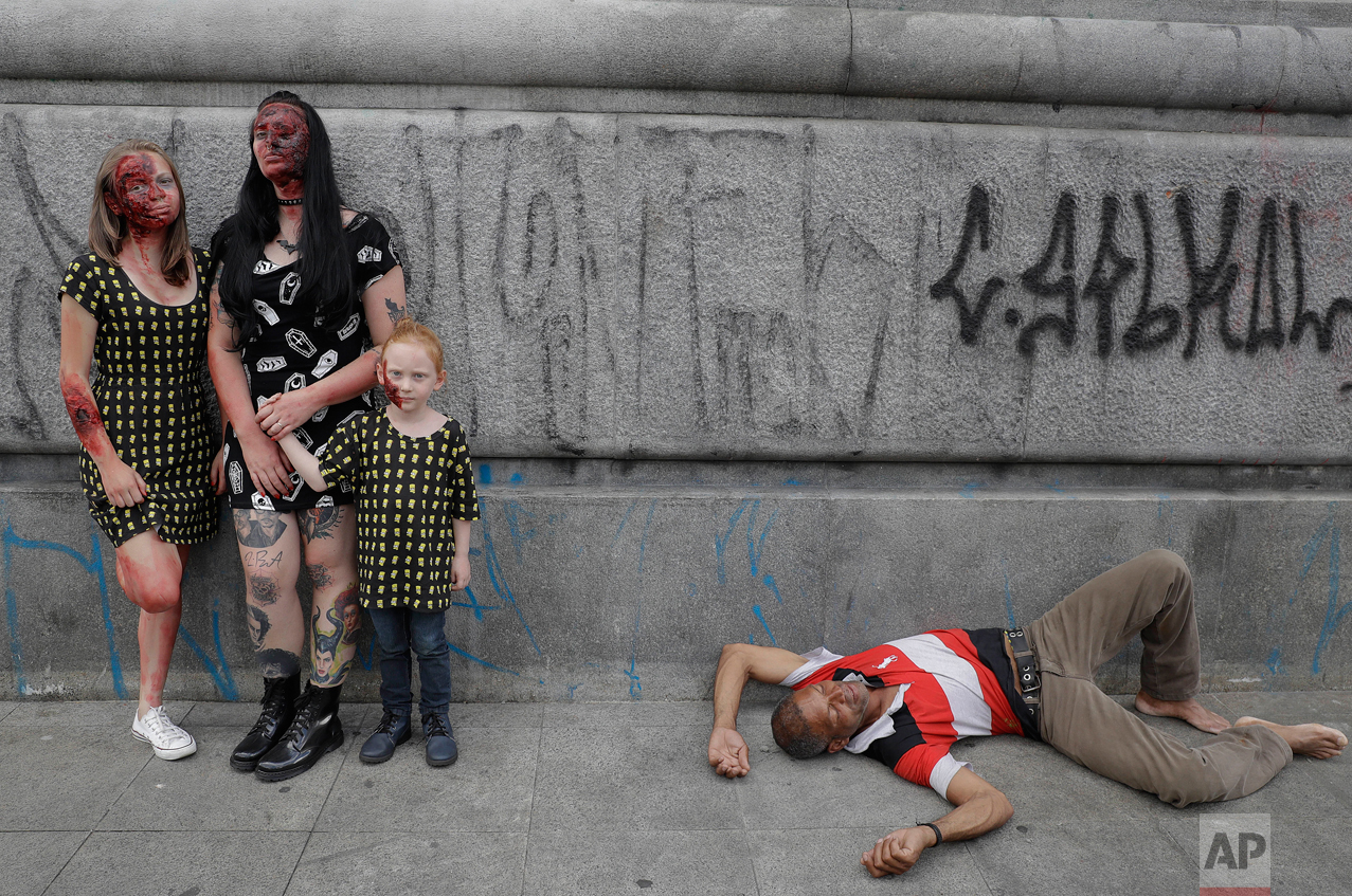  A family in zombie costumes pose for a picture as a man sleeps on the sidewalk at the Zombie Walk in Sao Paulo, Brazil, Wednesday, Nov. 2, 2016. Participants commemorated the Day of the Dead with the annual Zombie Walk. (AP Photo/Andre Penner) 