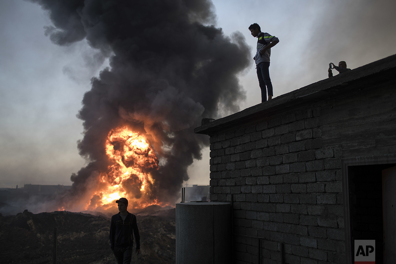  People watch as safety workers try to extinguish fires in a burning oil field in Qayara, south of Mosul, Iraq, Thursday, Nov. 3, 2016. A senior military commander says more than 5,000 civilians have been evacuated from newly-retaken eastern parts of