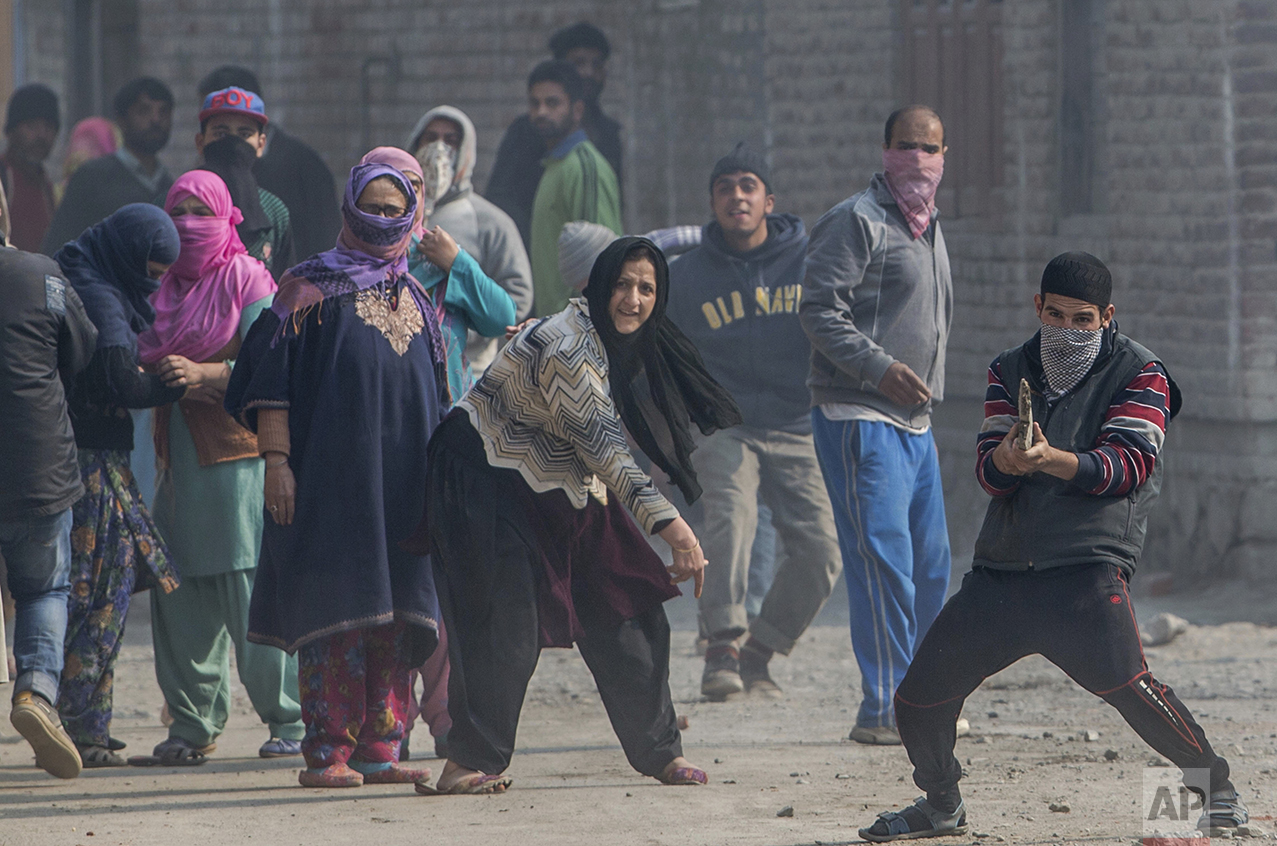  In this Wednesday, Nov. 2, 2016 photo, a Kashmiri Muslim protester, right, taunts Indian security personnel as a woman throws a stone at them during a raid carried out to arrest suspected protesters in the outskirts of Srinagar, Indian controlled Ka