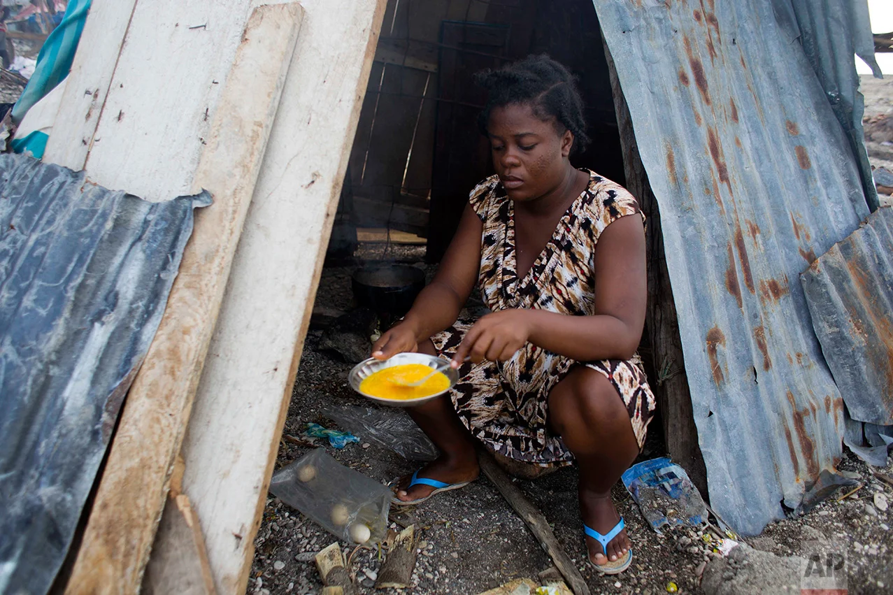 In this Nov. 1, 2016 photo, 19-year-old Nathanaelle Bernard, who is 7 months pregnant, cooks an omelet in a makeshift hut she is sharing with five members of her extended family, in Coteaux, Haiti. Hurricane Matthew destroyed her small home of cinder blocks and carried away most of her belongings, including the clothing and blankets she had managed to collect for her baby. (AP Photo/Dieu Nalio Chery)