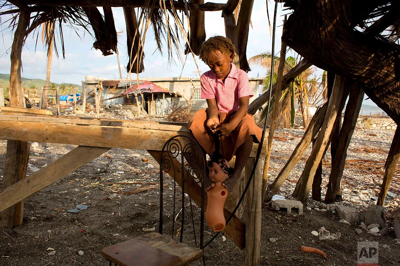 In this Oct. 31, 2016 photo, Roudiana Louis Pierre braids her doll's hair, near a field of debris where her home, destroyed by Hurricane Matthew, once stood in Coteaux, Haiti. The government says the storm killed 546 people and caused massive destruction of the crops and livestock. (AP Photo/Dieu Nalio Chery)