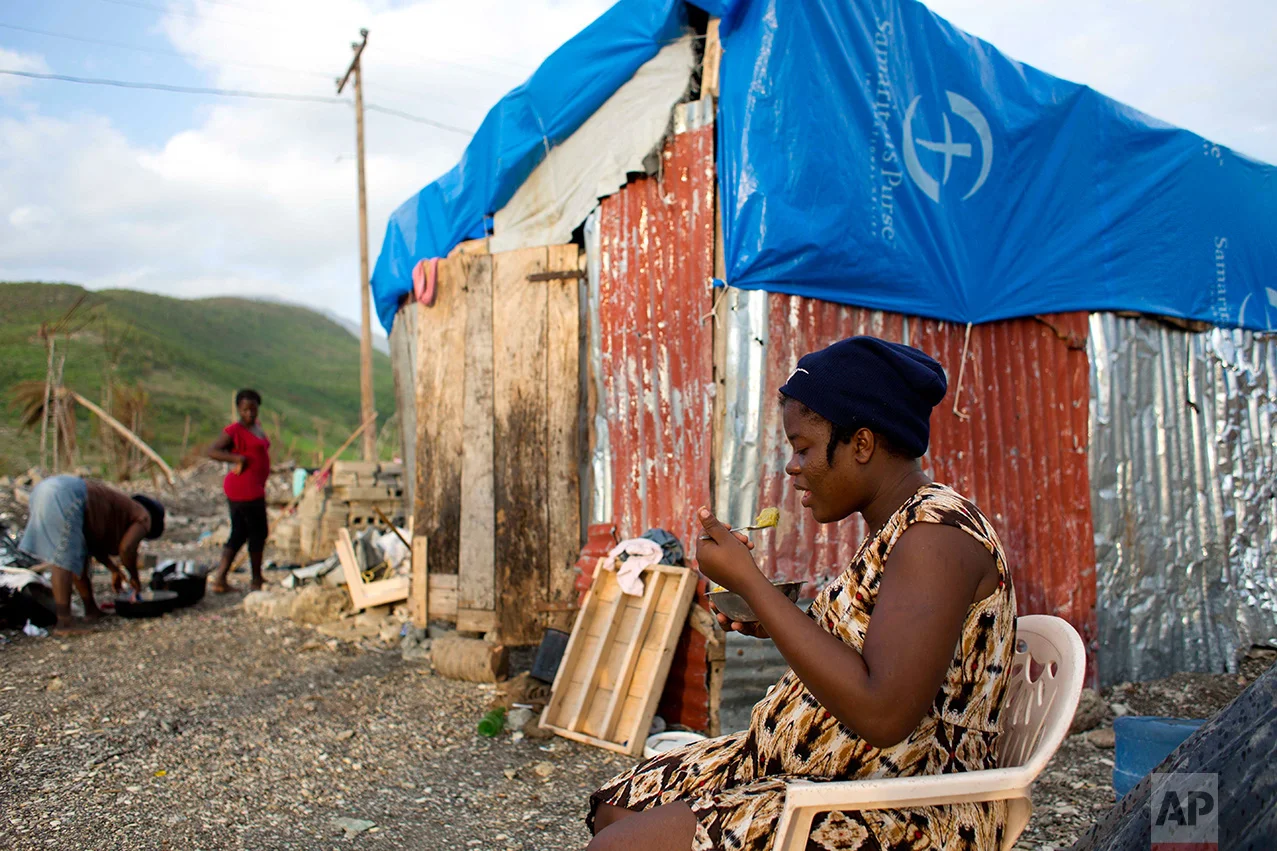 In this Oct. 31, 2016 photo, Nathanaelle Bernard, who is 7 months pregnant, eats a bowl of corn meal with bean paste, while sitting outside a makeshift hut she is sharing with five members of her extended family, in Coteaux, Haiti. "I worry most about nutrition," said Nathanaelle, "How can my baby be strong if I'm not eating well?" (AP Photo/Dieu Nalio Chery)
