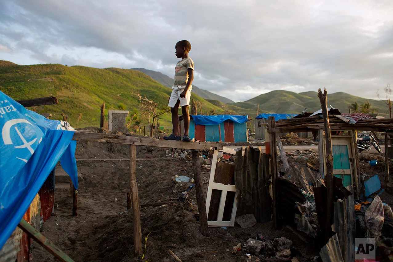 In this Nov. 1, 2016 photo, a boy stands on a wood frame of his home, destroyed by Hurricane Matthew, in Coteaux, Haiti. The storm crashed through his town overlooking the Caribbean Sea along the southwestern Haitian coast on Oct. 4, with 145 mph winds. (AP Photo/Dieu Nalio Chery)