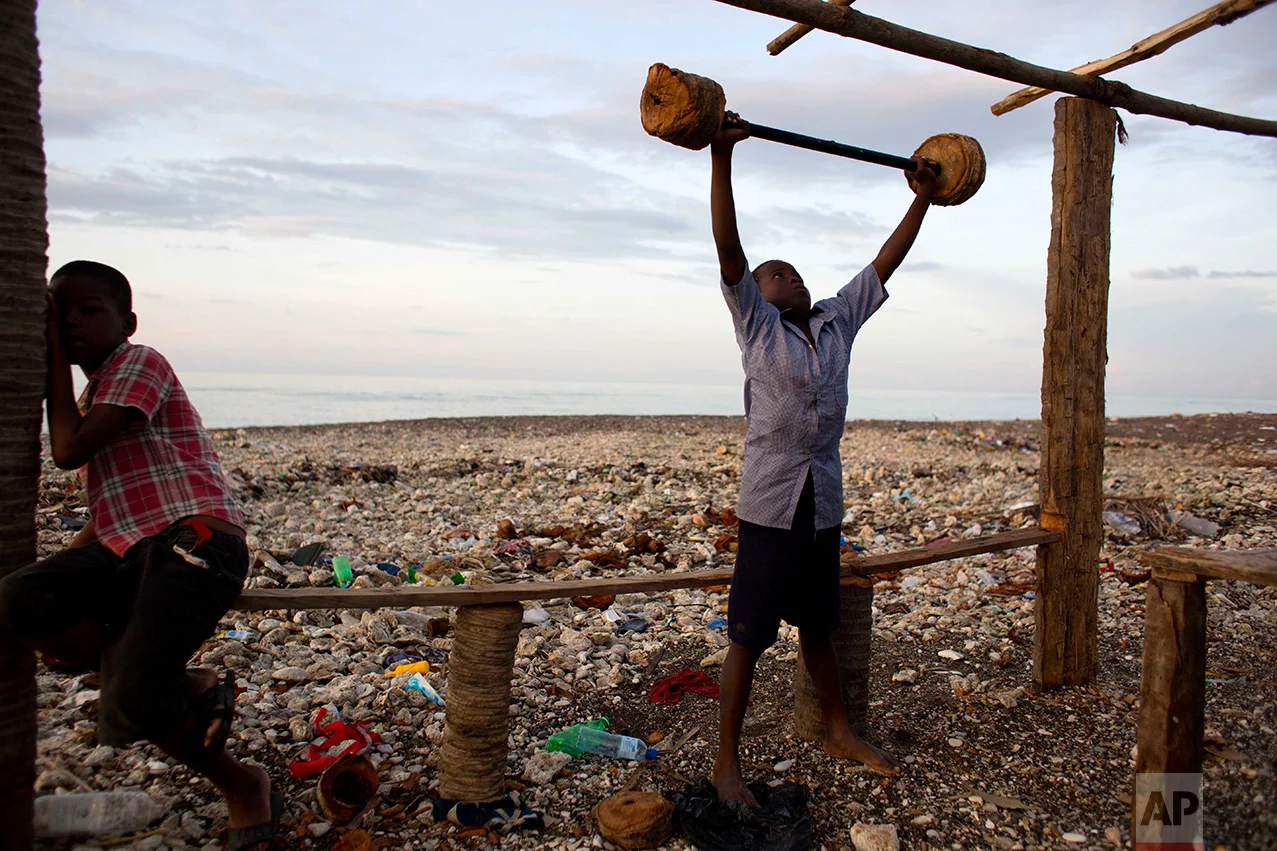 In this Nov. 1, 2016 photo, a boy lifts makeshift barbells near his home, destroyed by Hurricane Matthew, in Coteaux, Haiti. "It is tragic that a single storm can tear up so much of this progress, and that in a single day we can be set back by years," said Marielle Sander, representative for the U.N. Population Fund in Haiti. (AP Photo/Dieu Nalio Chery)