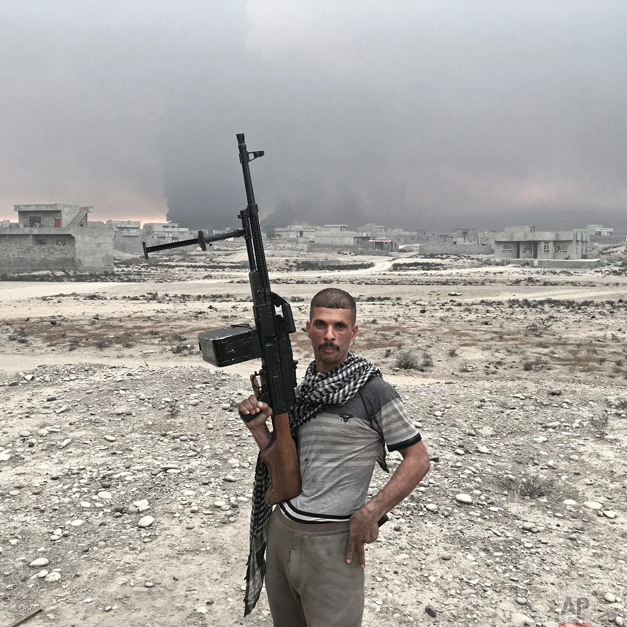 In this photo taken Sunday, Oct. 23, 2016, Haidar Hussein, 20, from Diwaniya, Iraq, an Iraqi army soldier, poses for a portrait while holding his machine gun on the outskirts of Qayara, some 50 kilometers south of Mosul, Iraq. The push to kick the Islamic State out of Mosul has brought together an eclectic mix of Iraqis, young and old, police and soldiers, and a variety of irregular uniforms and equipment. (AP Photo/Marko Drobnjakovic)