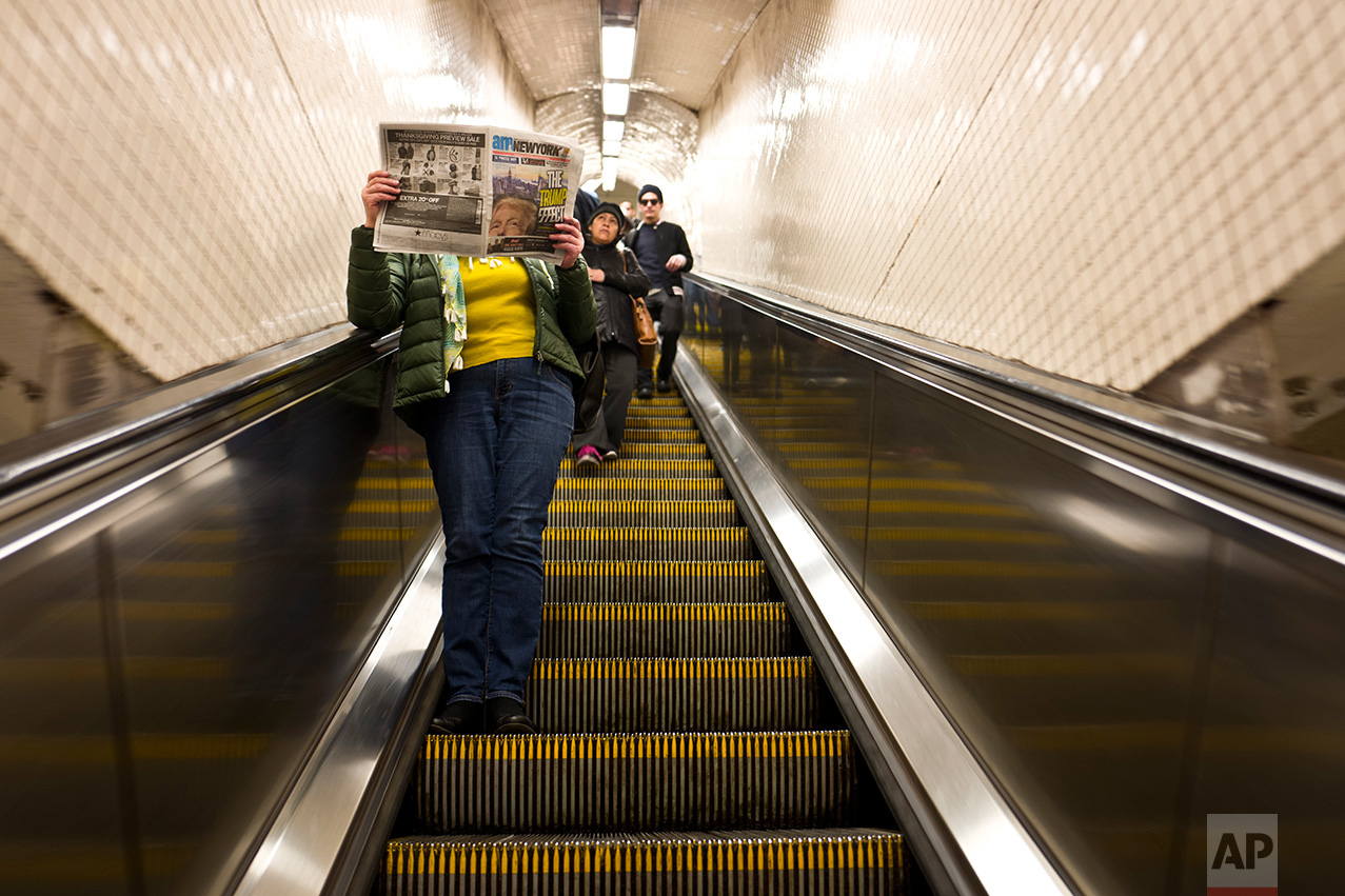 In this Monday, Nov. 14, 2016 photo, a woman reads a newspaper featuring on its front page an image of President-elect Donald Trump while going down an escalator of a subway station in New York. (AP Photo/Muhammed Muheisen)