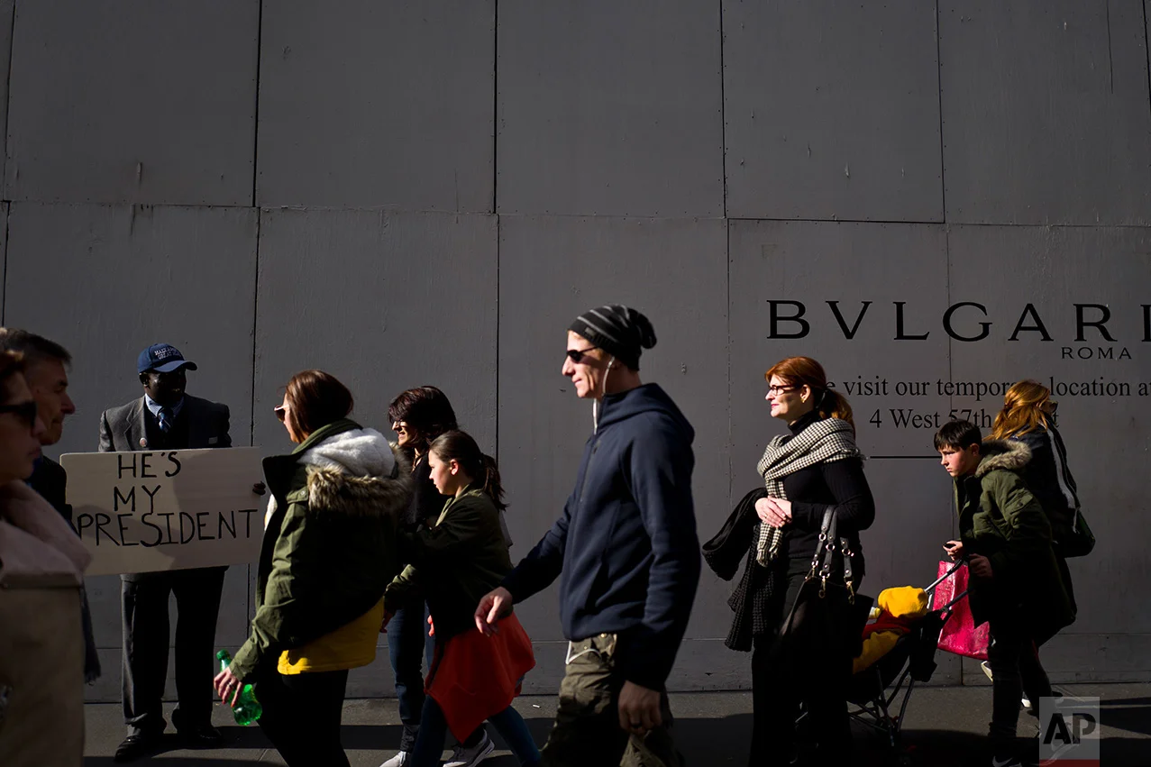 In this Monday, Nov. 14, 2016 photo, pedestrians pass a man holding a sign outside Trump Tower in New York. (AP Photo/Muhammed Muheisen)
