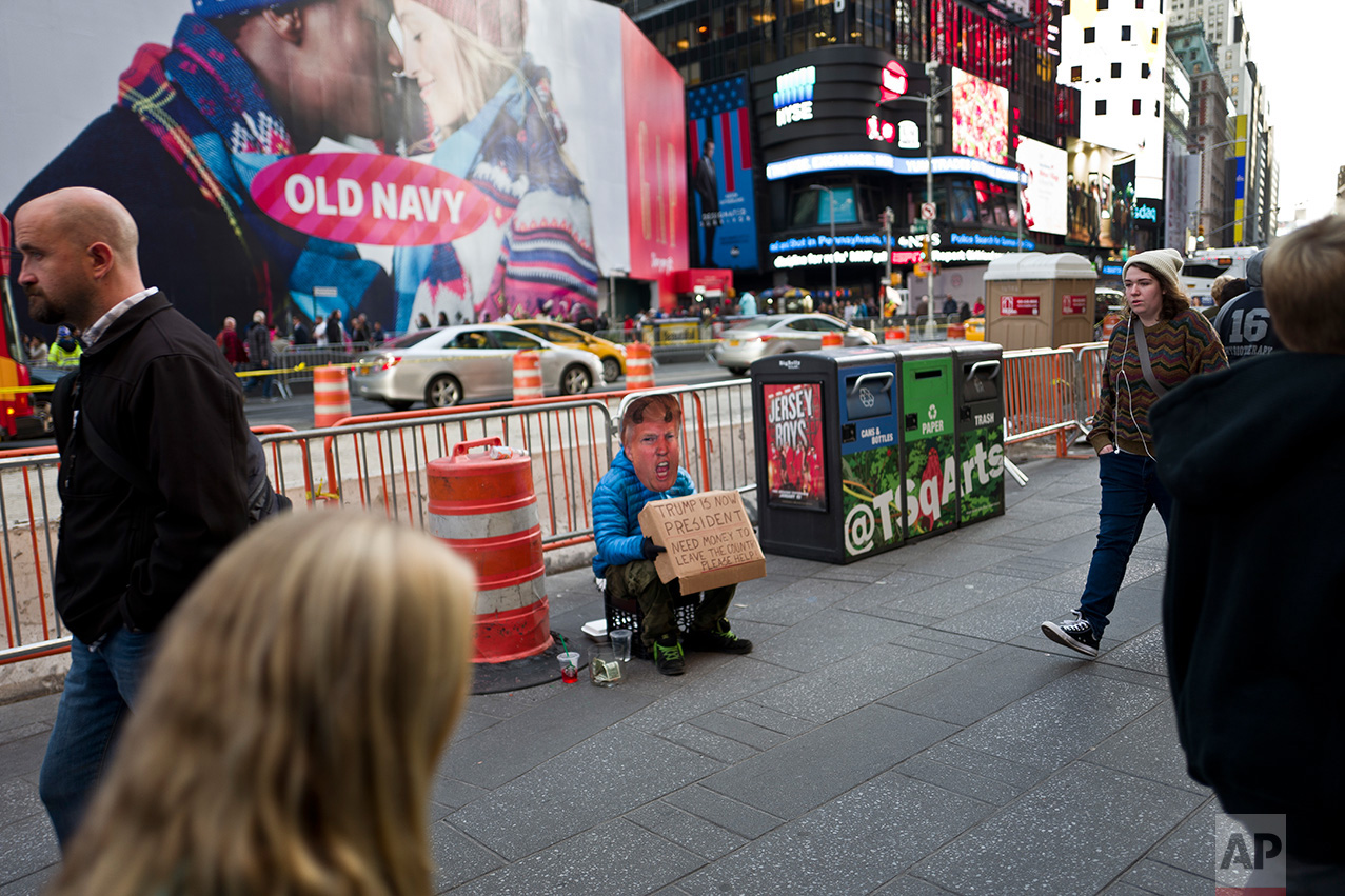 In this Thursday, Nov. 10, 2016 photo, a man wearing a mask showing President-elect Donald Trump sits on a sidewalk begging for money in New York. (AP Photo/Muhammed Muheisen)