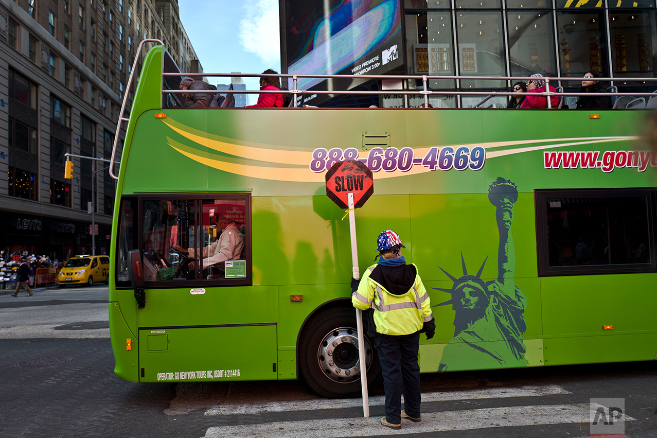 In this Thursday, Nov. 10, 2016 photo, a bus moves by a worker holding a sign in a crossroad in New York. (AP Photo/Muhammed Muheisen)