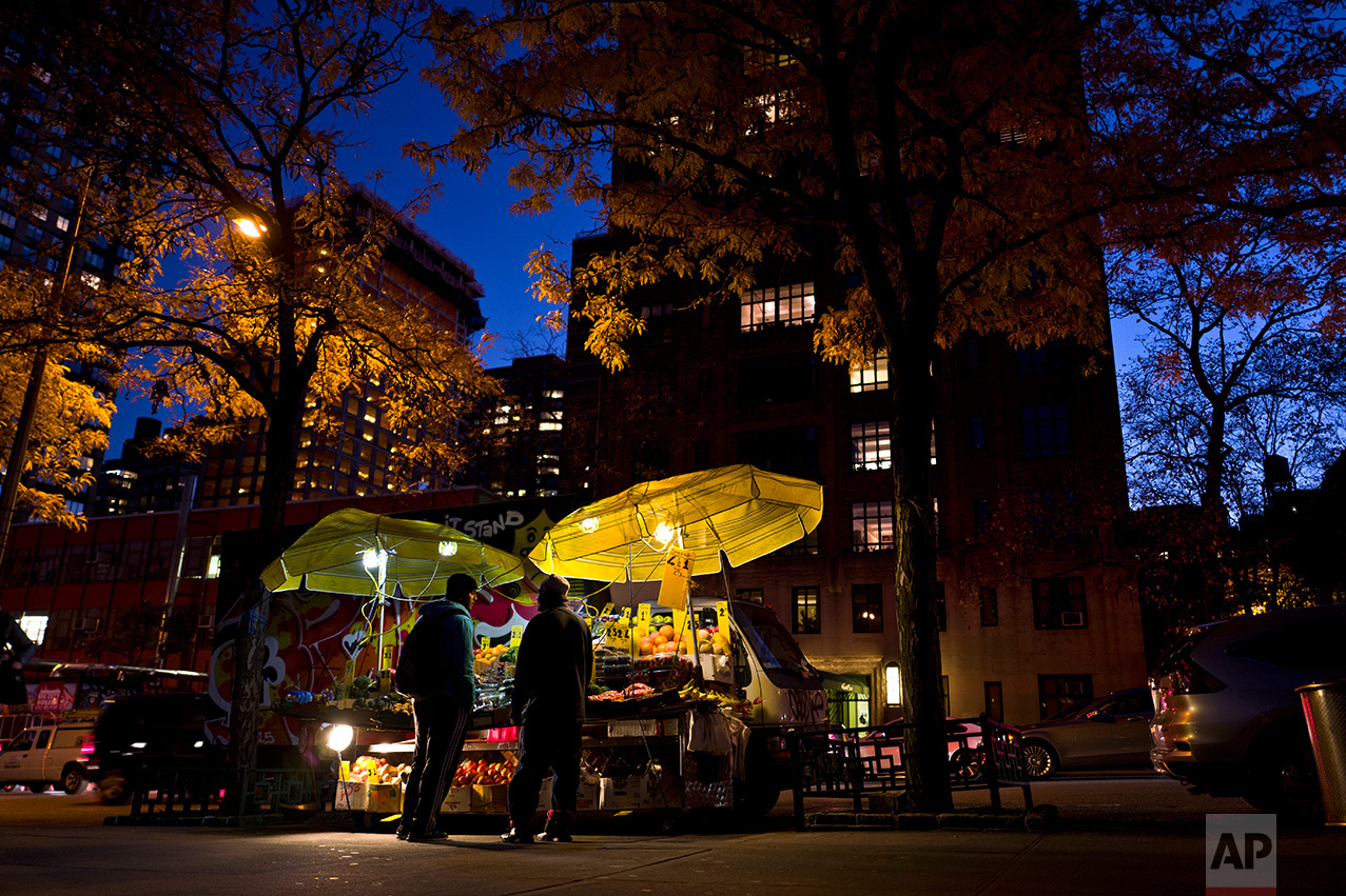 In this Thursday, Nov. 17, 2016 photo, a fruits and vegetables vendor, right, talks with a man while waiting for customers next to his stall on a roadside in New York. (AP Photo/Muhammed Muheisen)