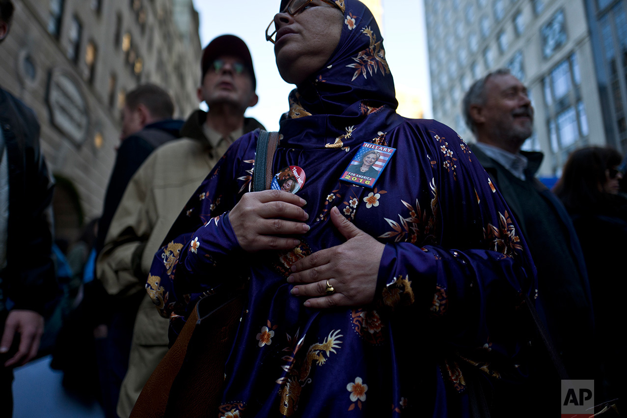 In this Sunday, Nov. 13, 2016 photo, a protestor wearing pins of support for Democratic presidential candidate Hillary Clinton, stands outside Trump Tower while she and others take part in a march against President-elect Donald Trump in New York. (AP Photo/Muhammed Muheisen)