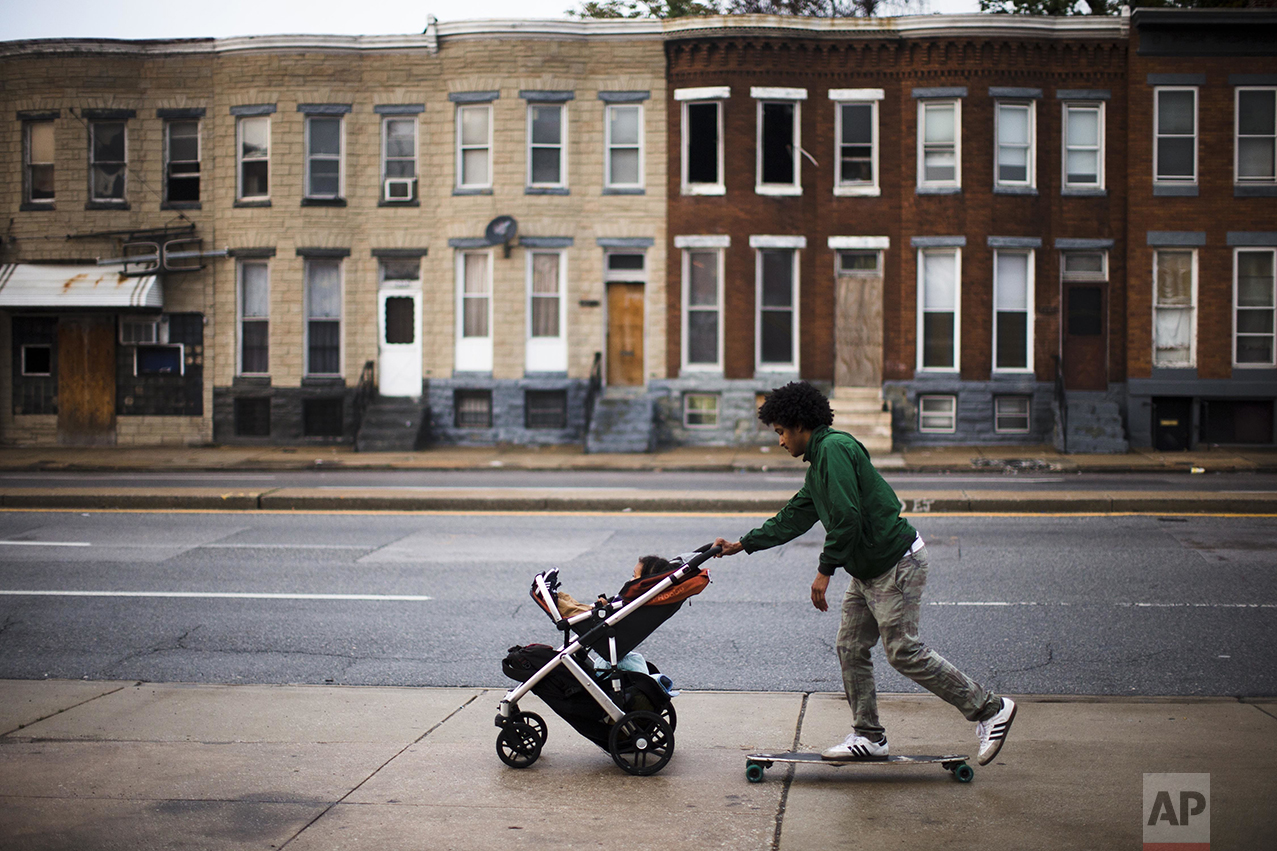 Carde Cornish, rides a skateboard as he takes his son, also named Carde, home past blighted buildings in Baltimore on Wednesday, May 11, 2016. Cornish, a young man who has spent his entire life in and around the Baltimore neighborhood where Freddie Gray lived and died, is socially and politicly engaged with the city around him. He works for Taharka Brothers, an ice-cream company with a social mission. "Our race issues aren't necessarily toward individuals who are white, but it is towards the system that keeps us all down, one, but keeps black people disproportionally down a lot more than anybody else," says Cornish. (AP Photo/Matt Rourke)