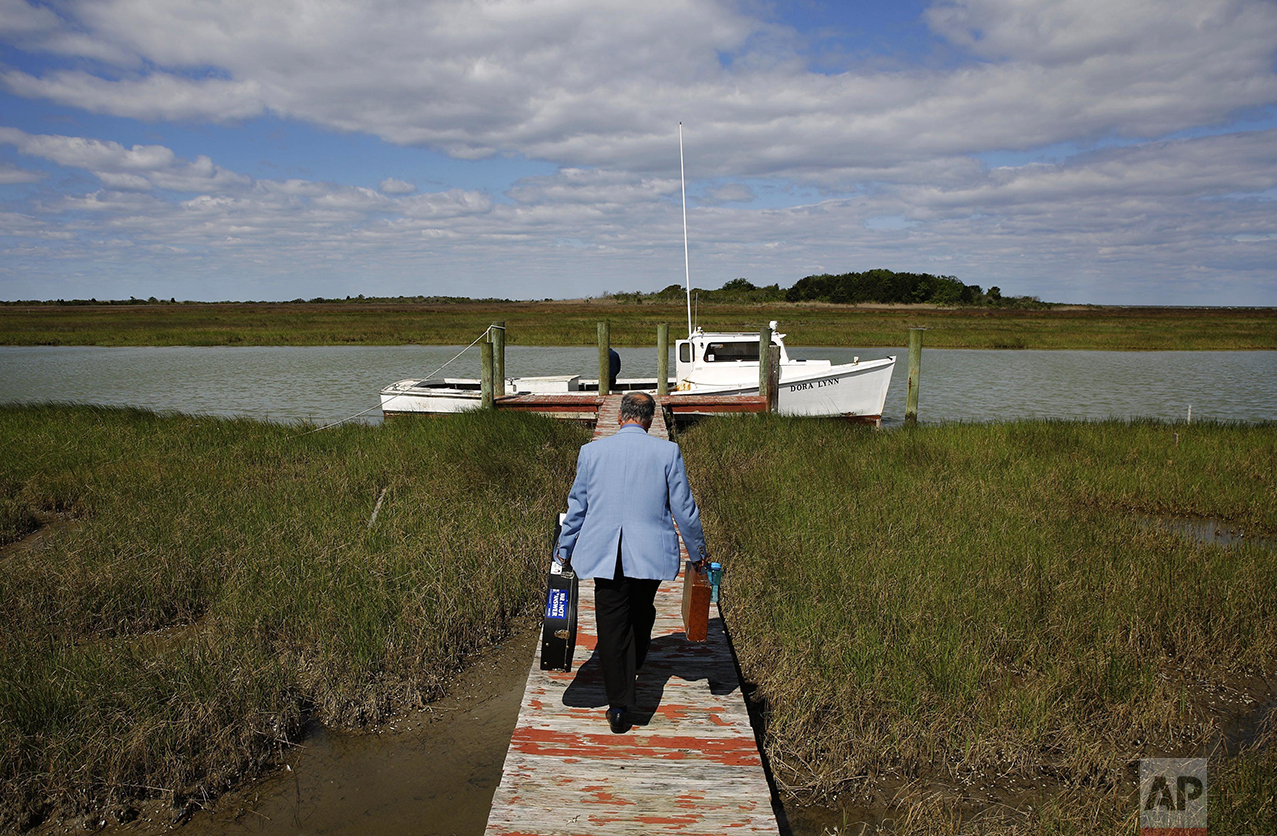 In this May 15, 2016 photo, Rev. Rick Edmund walks to a boat that will take him to a church service in the community of Tylerton on Smith Island, Md. As the pastor of the island's three United Methodist churches, he preaches in each one every Sunday, making his circuit by golf cart and boat. Located less than four hours from Washington, and perched in the middle of the Chesapeake Bay, Smith Island is so isolated that many of its residents still bear a unique accent that descended from its first European settlers 400 years ago. Its population, which has dwindled to a few hundred and is largely dependent on commercial fishing, is threatened by a combination of sea level rise and erosion. A sticker on his guitar case bears a quote by Native American Chief Seattle: "The Earth does not belong to us. We belong to the Earth." Edmund says the impact of climate change is going to be felt for centuries. (AP Photo/Patrick Semansky)
