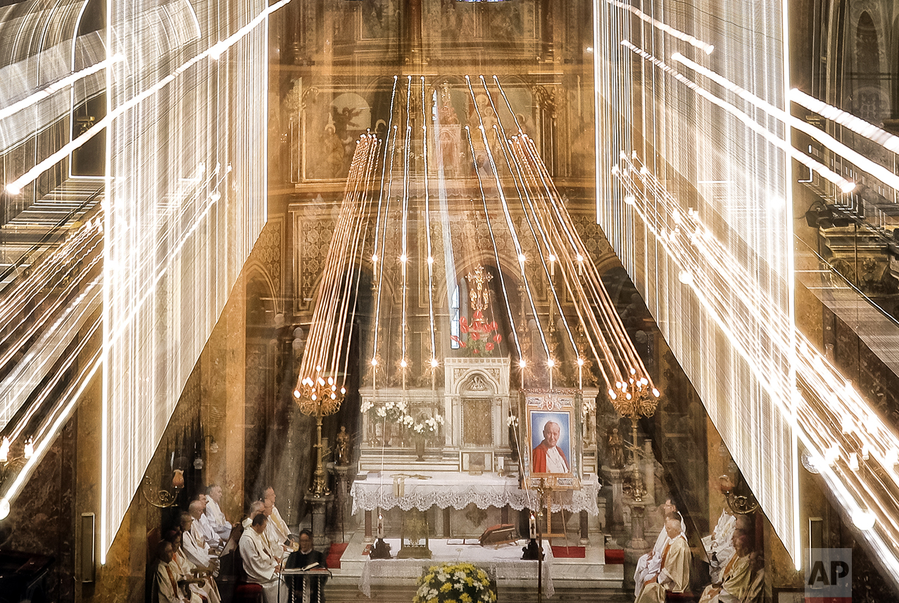  In this Sunday, Oct. 23, 2016 picture taken with a long exposure time, Catholic priests sit inside the St. Joseph cathedral next to remains and an icon depicting Pope John Paul II during a pilgrimage, in Bucharest, Romania. (AP Photo/Vadim Ghirda) 