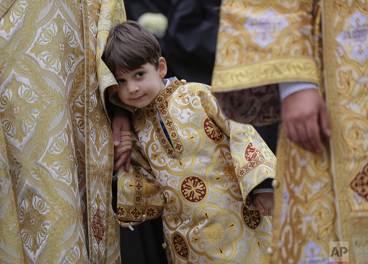  In this Saturday, Oct. 22, 2016 picture, a child wearing a priest outfit holds the hand of an Orthodox priest before a pilgrimage, in Bucharest, Romania. Both churches parade holy remains. The Catholics have a few drops of the blood of Saint John Pa