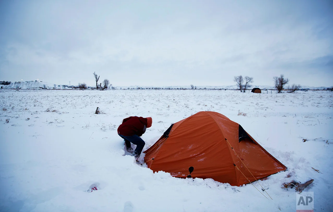 In this Wednesday, Nov. 30, 2016 photo, Roy Tom of Ontario, Canada, and a member of the Ojibwa Native American tribe clears away snow from his tent where he's lived for over two months at the Oceti Sakowin camp where people have gathered to protest the Dakota Access oil pipeline, in Cannon Ball, N.D. "You have to get used to it," Tom said of the snow and cold weather. (AP Photo/David Goldman)